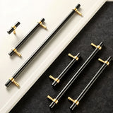 "Set of black and gold brass pull bars with cylindrical design and subtle accents, arranged on a white and dark grey surface."