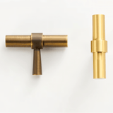 "Two styles of gold and antique brass pull bars with cylindrical design, lying side by side on a white background."