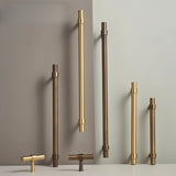 "Set of gold and antique brass pull bars with cylindrical design and subtle accents, arranged on a grey and white surface."