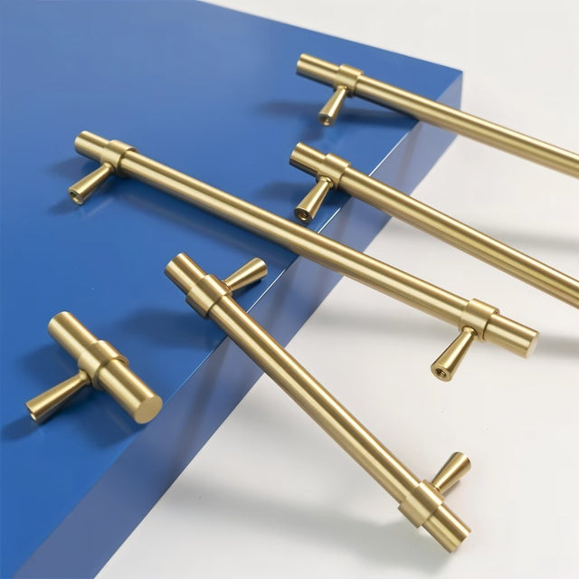"Gold brass pull bars with cylindrical design and subtle accents, arranged on a blue and white surface."