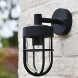 "Black Siam outdoor wall lamp with a cylindrical glass casing, showing the full fixture against a textured brick wall."