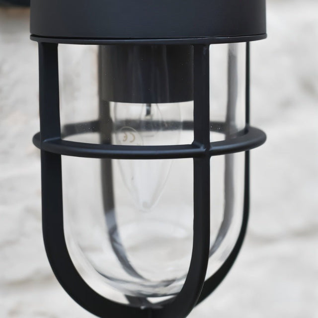 "Close-up of a black Siam outdoor wall lamp showing the protective cylindrical glass casing and light bulb."