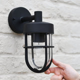 "Hand adjusting a black Siam outdoor wall lamp with a cylindrical glass casing, mounted on a textured brick wall."