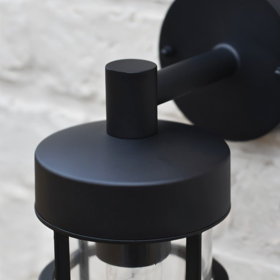 "Close-up top view of a black Siam outdoor wall lamp showing the cylindrical glass casing and wall mount."