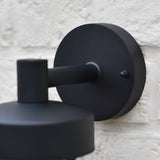 "Close-up of a black circular wall mount for a Siam outdoor wall lamp against a textured wall."