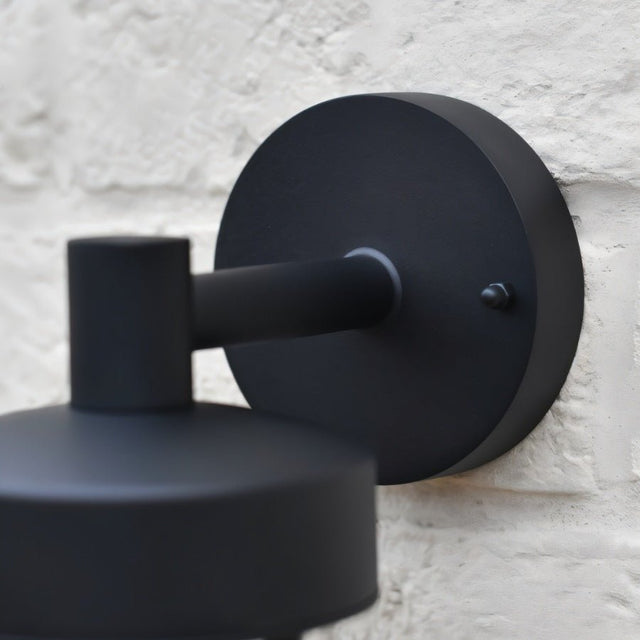 "Close-up of a black circular wall mount for a Siam outdoor wall lamp against a textured wall."