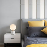 Sibwa Table Lamp with white base on a bedside table, casting warm light in a modern bedroom with grey and yellow bedding.