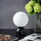 Sibwa Table Lamp with glossy black base and glowing globe beside a flower vase, ideal for stylish home or office lighting.