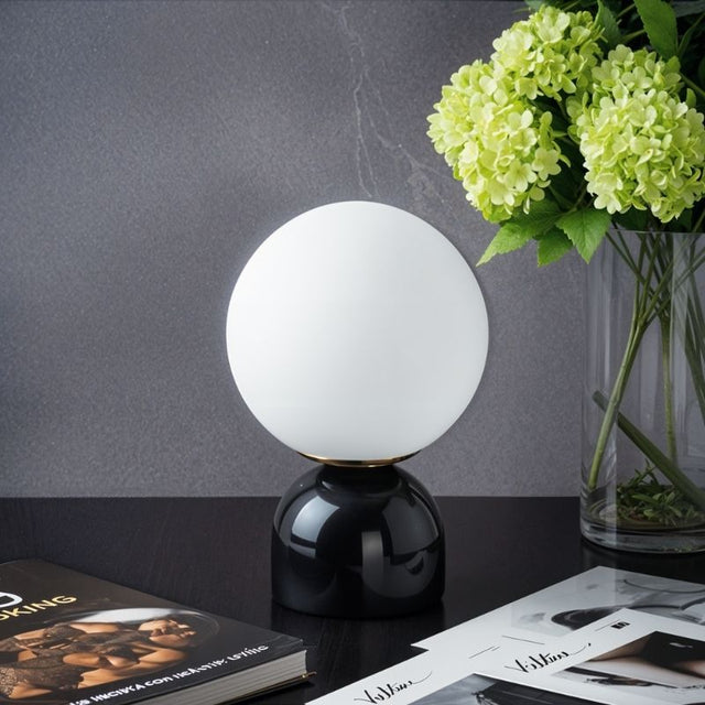 Sibwa Table Lamp with glossy black base and glowing globe beside a flower vase, ideal for stylish home or office lighting.