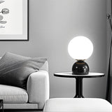 Sibwa Table Lamp on a black side table in a grey-toned living room, offering elegant ambient lighting with a modern touch.