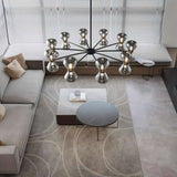 "Black iron Silvine chandelier with smoked glass spherical shades hanging above a modern living room with a grey sofa and marble coffee tables."
