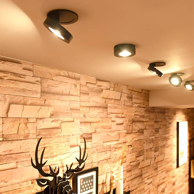 Black recessed LED downlights mounted on white ceiling above stacked stone brick wall.