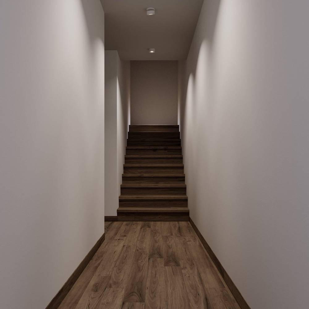 Recessed ceiling light fixture installed in a narrow hallway with white walls and wooden stairs.