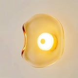 "Close-up of a modern wall lamp with a fluid, amber glass shade and a glowing light."