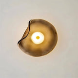 "Close-up of a modern wall lamp with a fluid, amber glass shade and a glowing light."