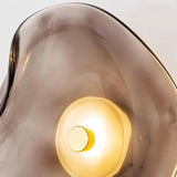 "Close-up of a modern wall lamp with a fluid, smoky grey glass shade and a warm, glowing light."