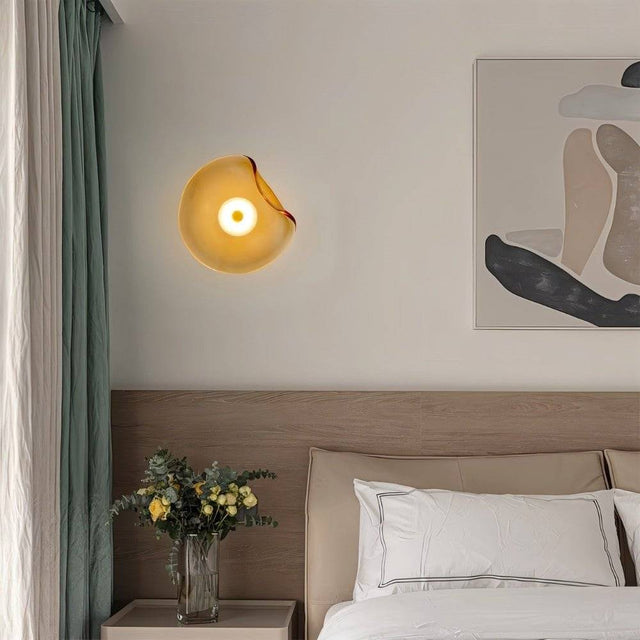 "Modern wall lamp with an amber, fluid-shaped glass shade and iron base illuminating a contemporary bedroom."