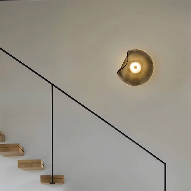 "Modern wall lamp with a fluid, grey glass shade and iron base illuminating a contemporary hallway with a staircase."