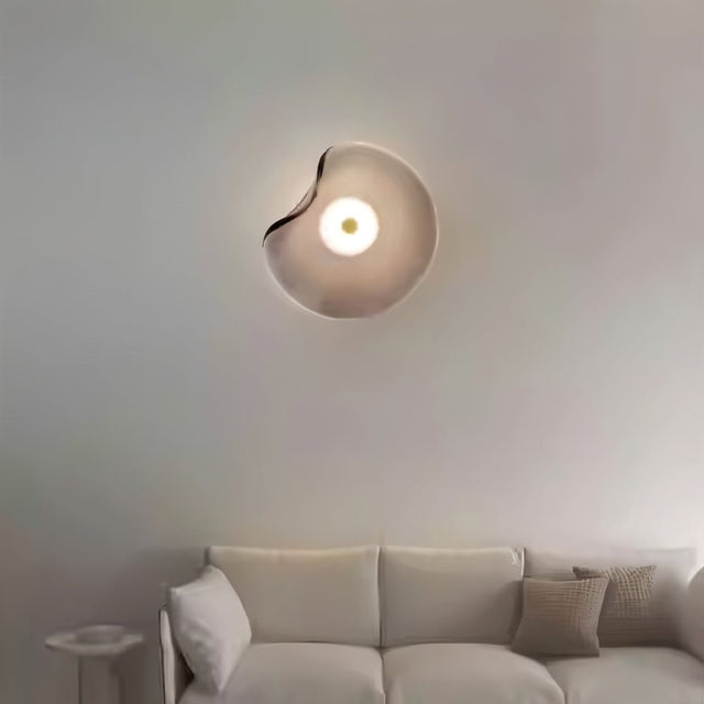 "Modern wall lamp with a fluid, grey glass shade and iron base casting a soft glow in a minimalist living room."