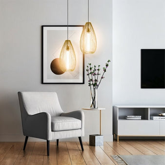 "Two amber glass pendant lights with teardrop-shaped open wire frames hanging above a modern armchair in a contemporary room."