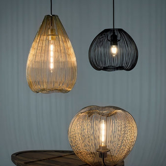 "A trio of pendant lights with open wire frames, one amber teardrop-shaped, one amber rounded, and one black rounded."