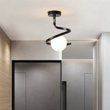 "A modern black ceiling light with a spiral frame and frosted glass globe in a contemporary hallway with gray walls and a door."