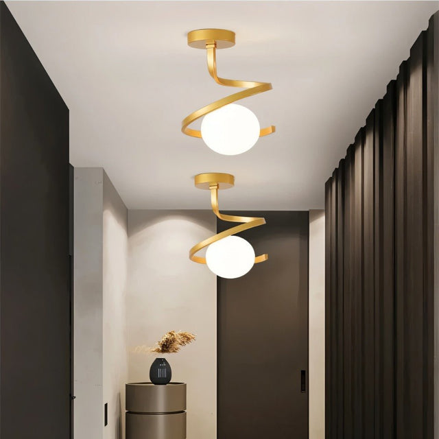 "Two modern gold ceiling lights with spiral frames and frosted glass globes in a contemporary hallway with dark doors and walls."