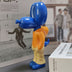 Colorful plastic figurine with blue head and limbs, yellow torso, and orange middle section displayed on desk.