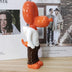 Glossy red and white ceramic figurine with brown pants displayed on wooden surface near interior design magazines.
