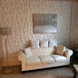 Someni Wall Panel installed in a modern living room, featuring a 3D geometric PVC design behind a white tufted sofa.