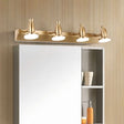 "A modern, 4-head vanity light in a brushed gold finish mounted above a bathroom mirror cabinet."