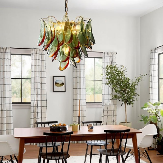 "Murano glass chandelier with green and red accents, hanging above a wooden dining table in a bright dining room."