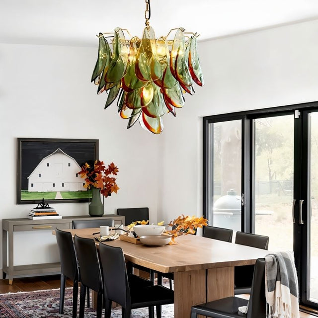  "Murano glass chandelier with green and red accents, hanging above a wooden dining table in a modern dining room with artwork."