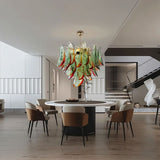 "Murano glass chandelier with green and red accents, hanging above a round dining table in a modern dining room with stairs."