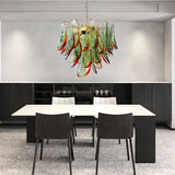"Murano glass chandelier with green and red accents, hanging above a modern dining table and chairs."