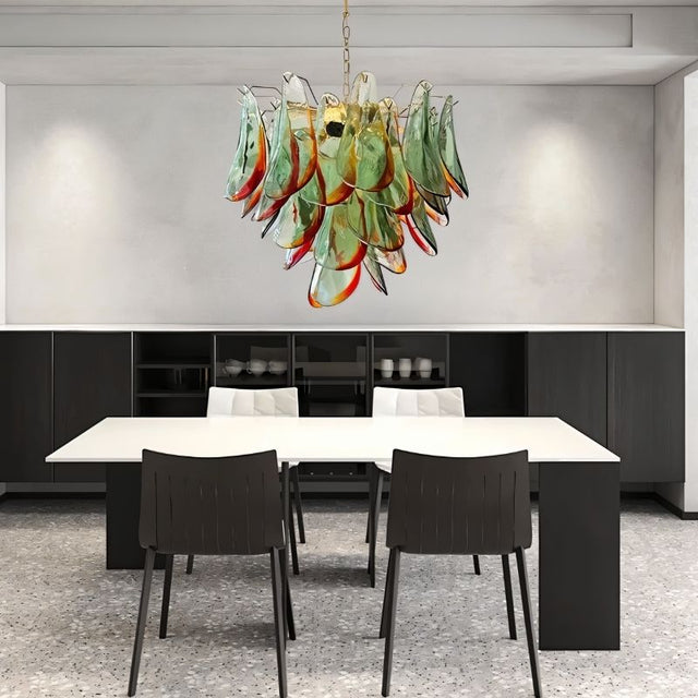 "Murano glass chandelier with green and red accents, hanging above a modern dining table and chairs."