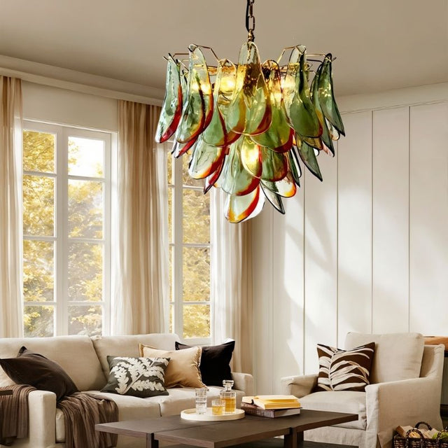 "Murano glass chandelier with green and red accents, hanging in a living room with a sofa and large windows."