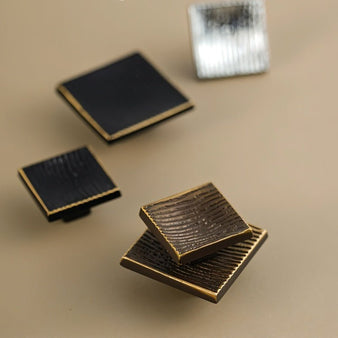 "Close-up studio shot of square brass cabinet knobs with a textured, ridged surface on a neutral background."