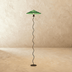 Black serpentine floor lamp with pleated cream fabric shade, studio white background with art poster and trailing plant.
