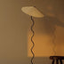 Floor lamp with curved black stem and pleated cream-colored shade casting warm light against neutral wall.