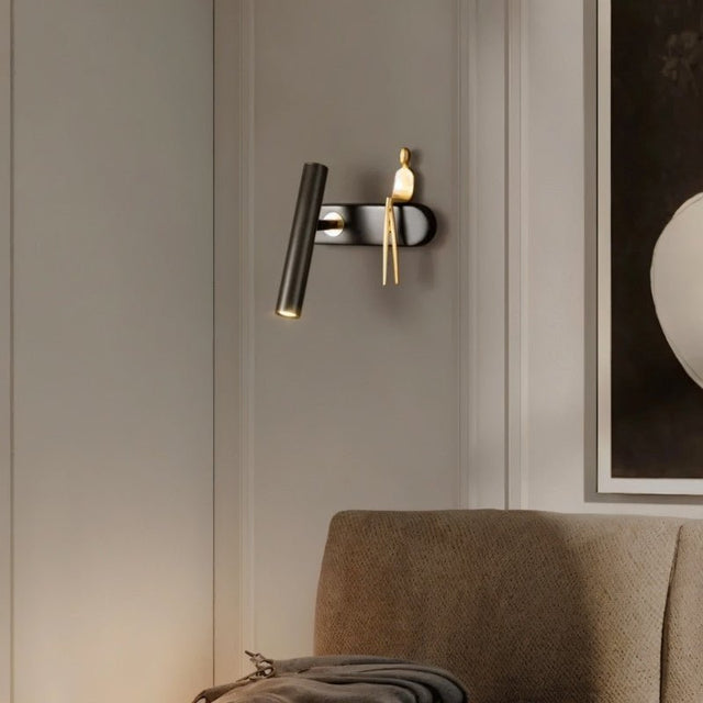 "A black and gold bedside reading lamp with a figurine on a living room wall."