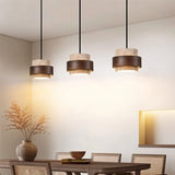"Group of three modern stone and wood cylindrical pendant lights hanging over a dining table."