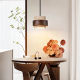 "Modern stone and wood cylindrical pendant light hanging over a round dining table with flowers and chairs."