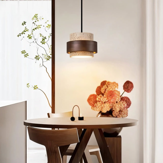 "Modern stone and wood cylindrical pendant light hanging over a round dining table with flowers and chairs."