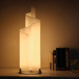 Stellora Table Lamp glowing warmly on a shelf beside books, offering integrated LED lighting for cozy modern interiors.