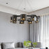 Modern black metal chandelier with gold-accented cylindrical shades suspended above a gray sectional sofa.