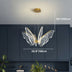 Butterfly-shaped pendant chandelier with brass finish and LED wing details suspended above dark cabinetry.