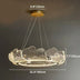 Modern brass pendant chandelier with shell-shaped acrylic diffusers, suspended against a neutral wall.