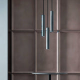 "Three gray cylindrical pendant lights hanging above a round table in a dining area with a textured, brown wall."
