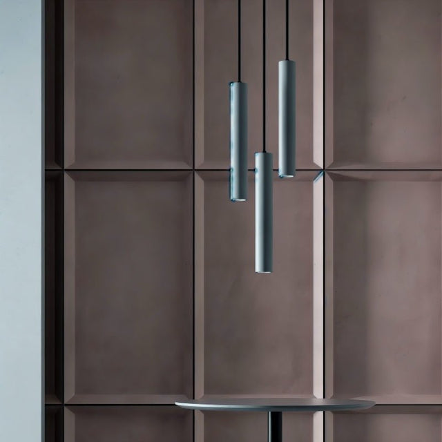 "Three gray cylindrical pendant lights hanging above a round table in a dining area with a textured, brown wall."